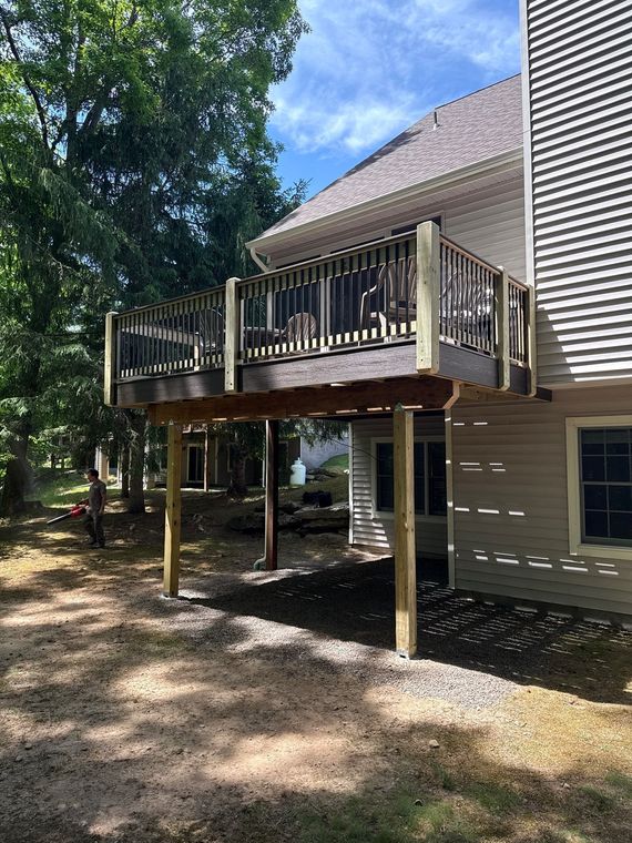 Raised wooden deck beside beige house in a wooded yard under a blue sky