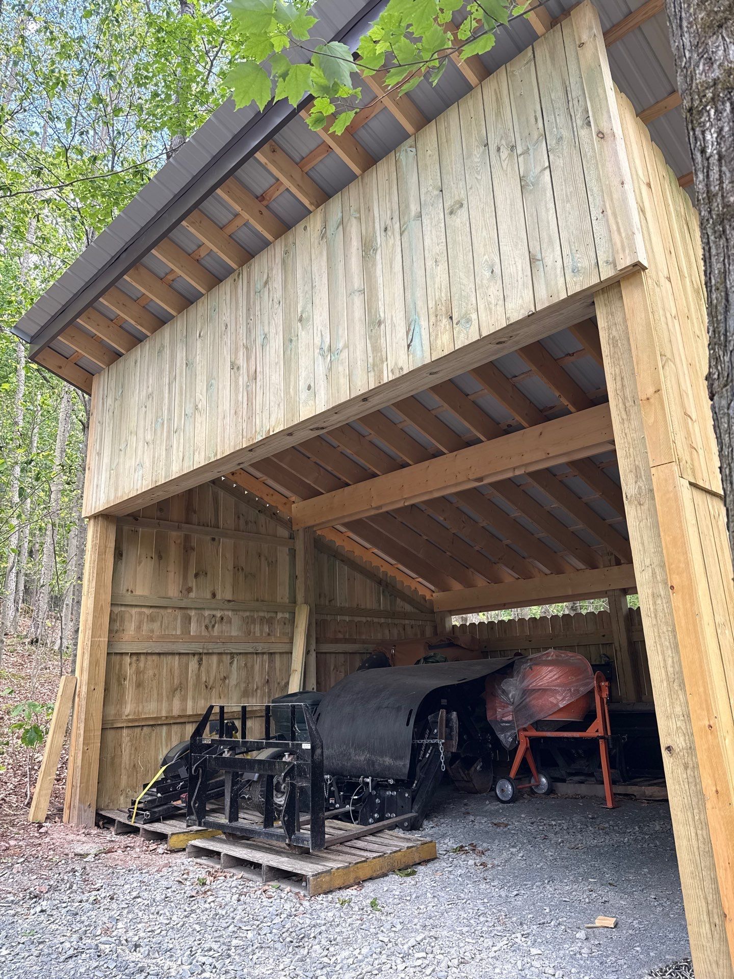 Open wooden garage with parked equipment and a red grill inside