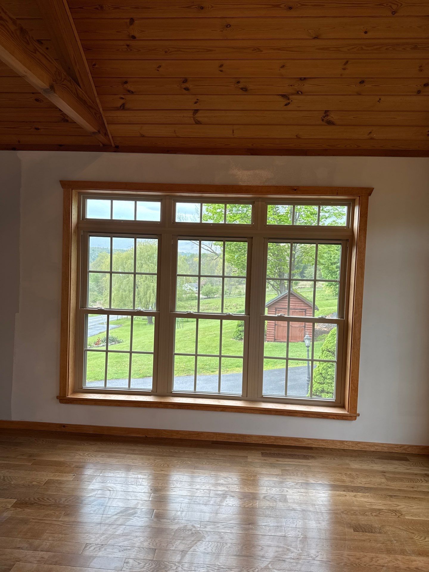 Empty wooden room with a large window overlooking trees and a red shed