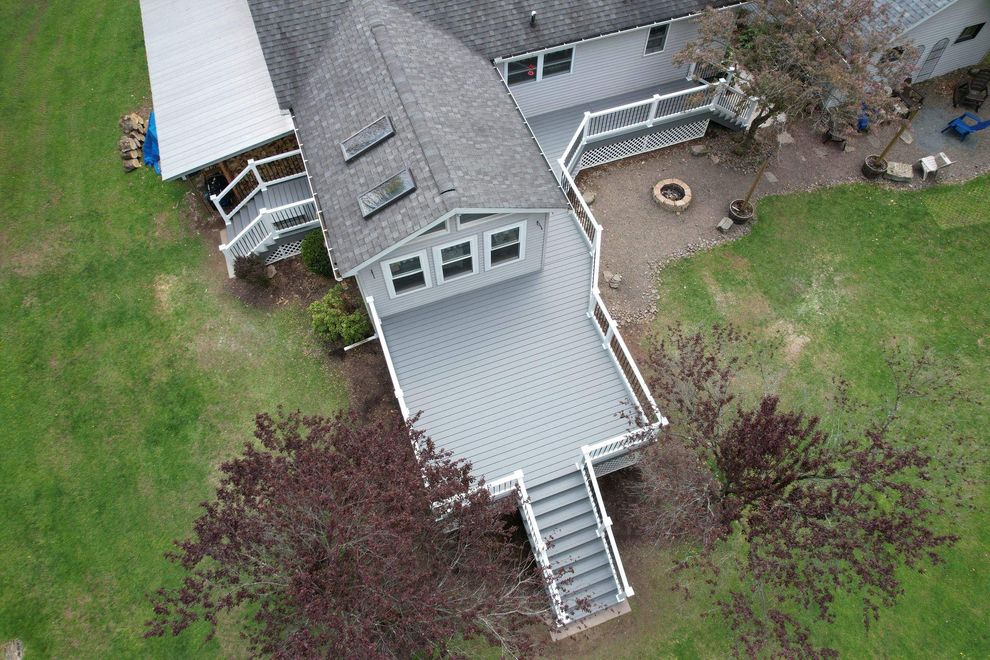 Aerial view of a gray house with a deck, stairs, and landscaped yard.