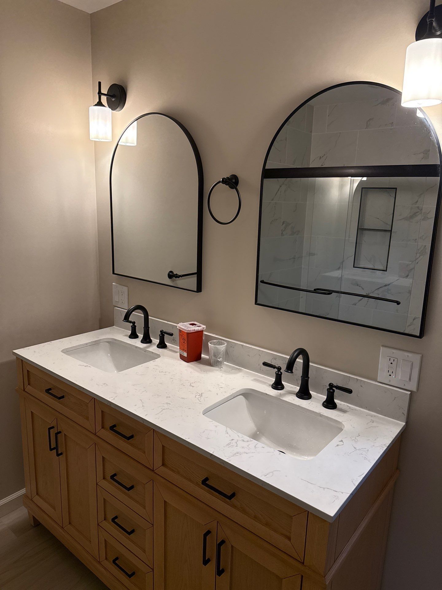 Bathroom vanity with double sinks, black fixtures, oval mirrors, and warm wood cabinets