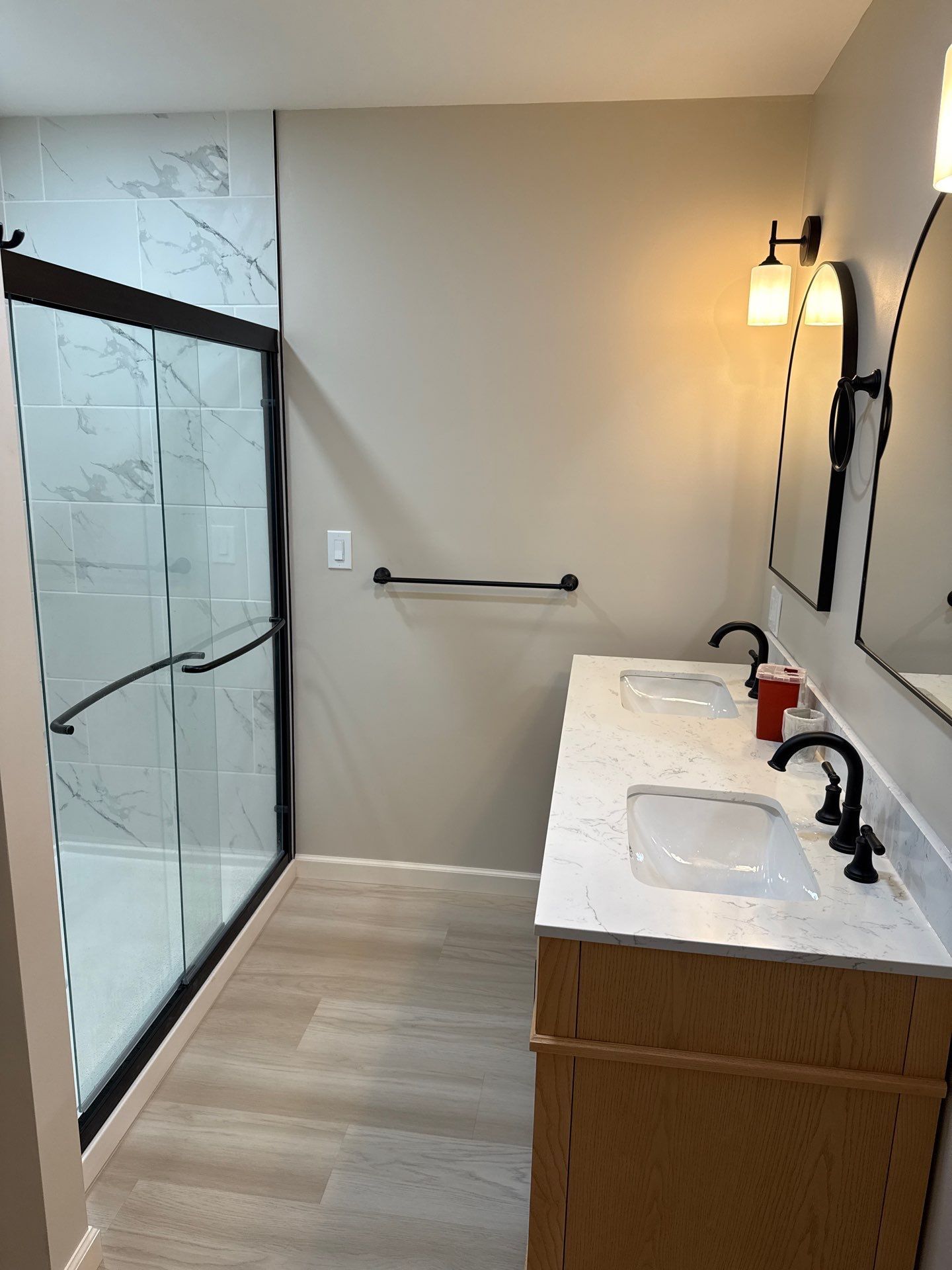 Modern bathroom with glass shower, double sink vanity, beige walls, and black fixtures