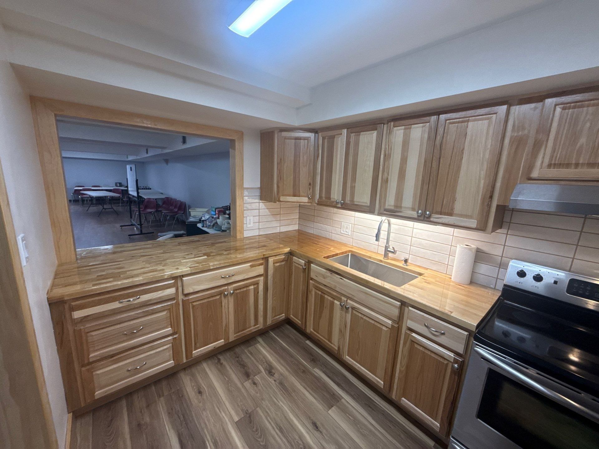 Compact kitchen with wood cabinets, tiled backsplash, stainless oven, and pass-through opening to dining area
