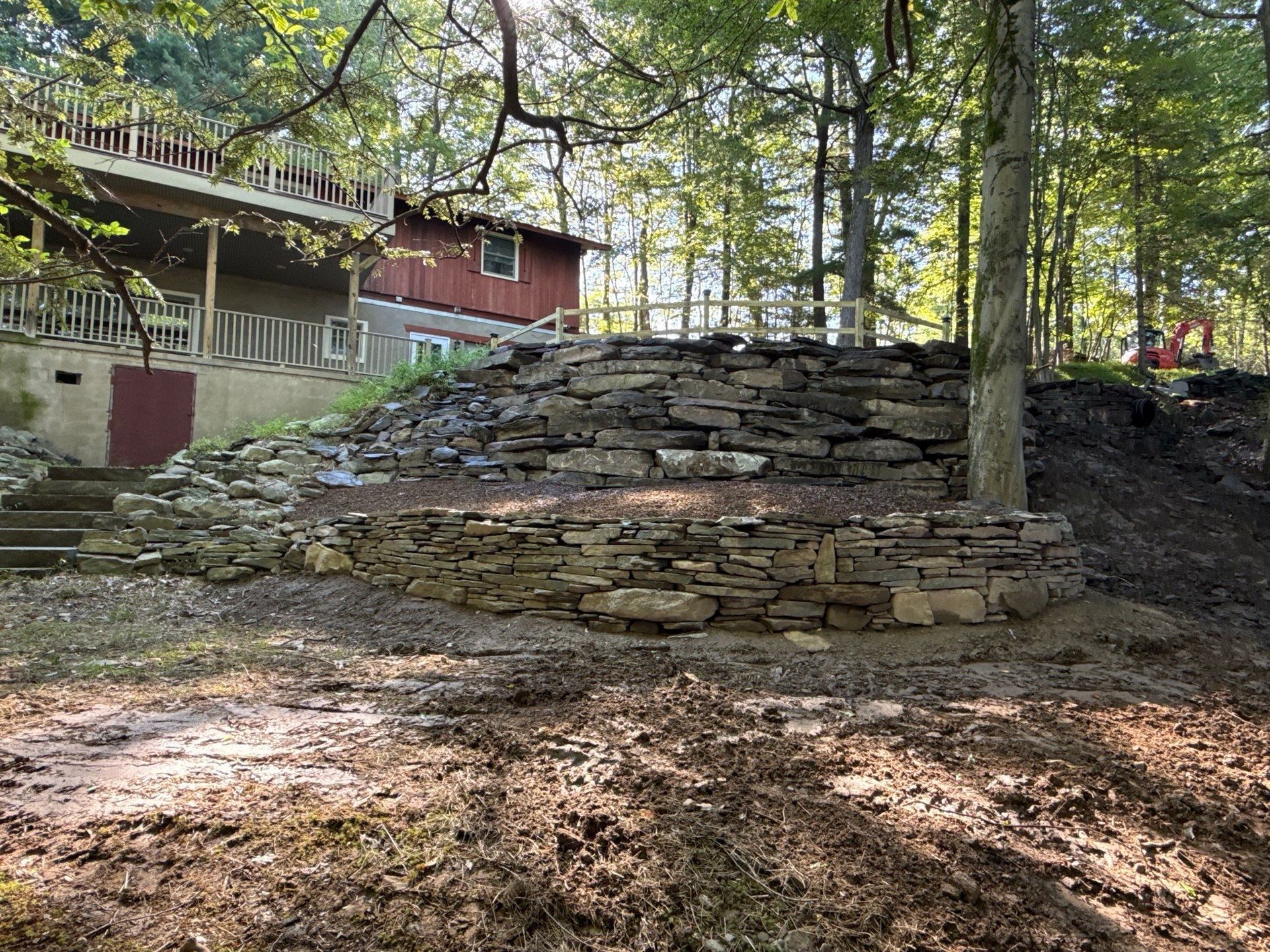 Stone retaining wall in a wooded park beside a red cabin and steps on a sunny day