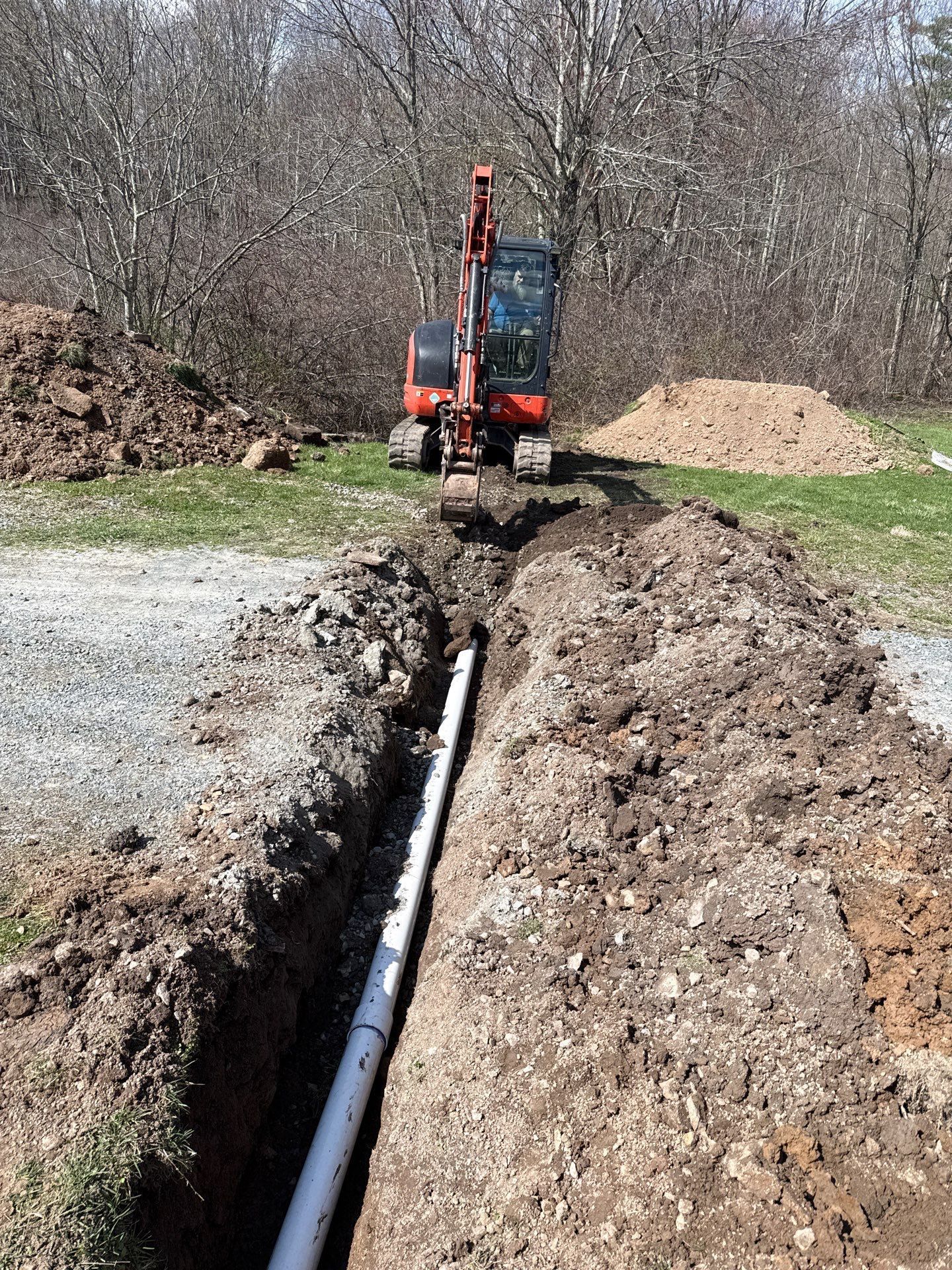 Excavator digging a trench in a field with a black pipe laid along the bottom
