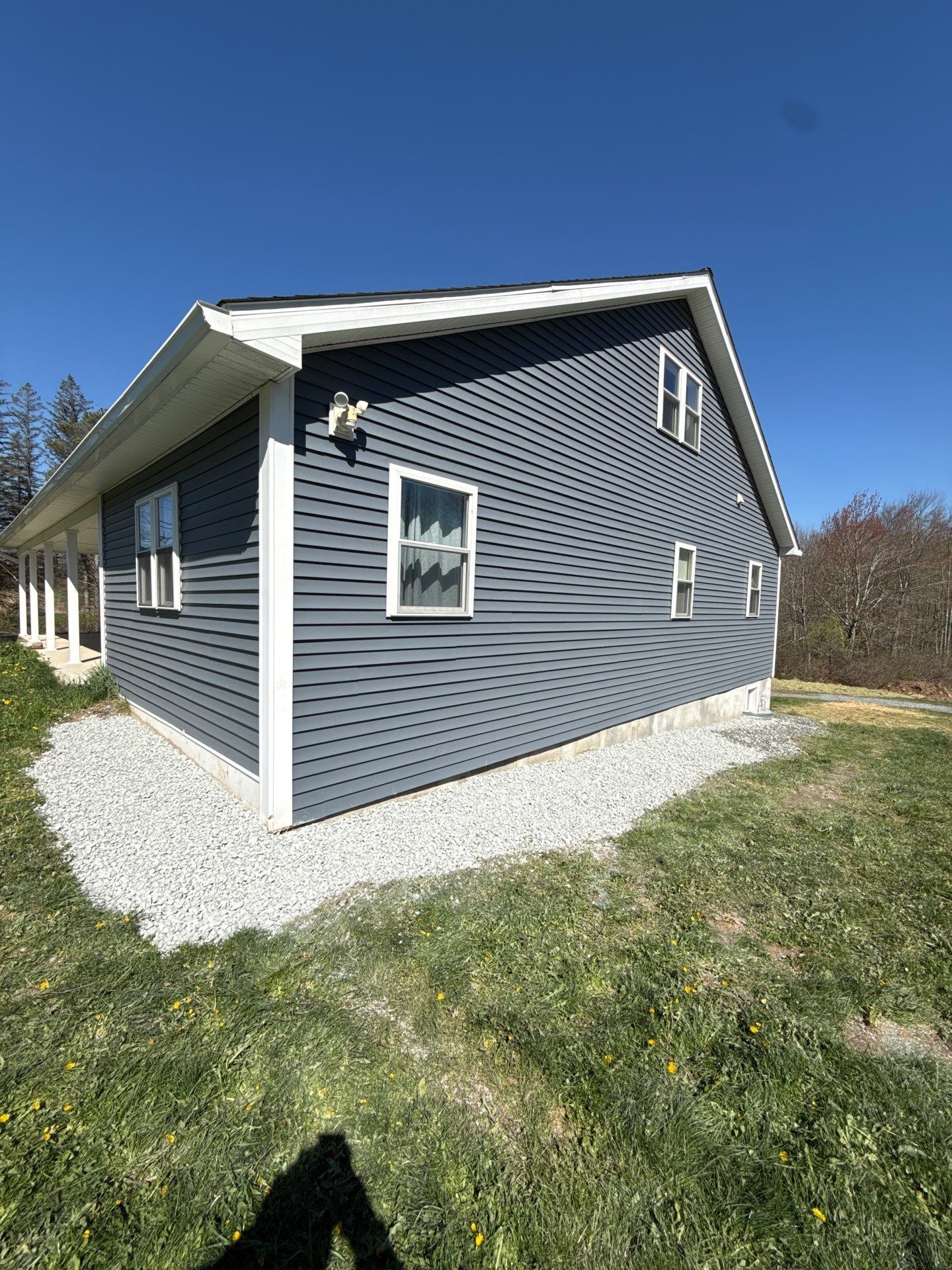 Gray-sided house with white trim and gravel foundation, viewed from the backyard on a sunny day