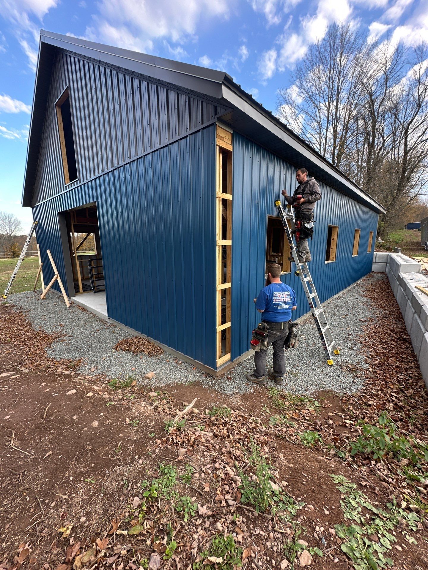 Blue metal-sided building with two people climbing on the exterior and a child standing below outdoors.