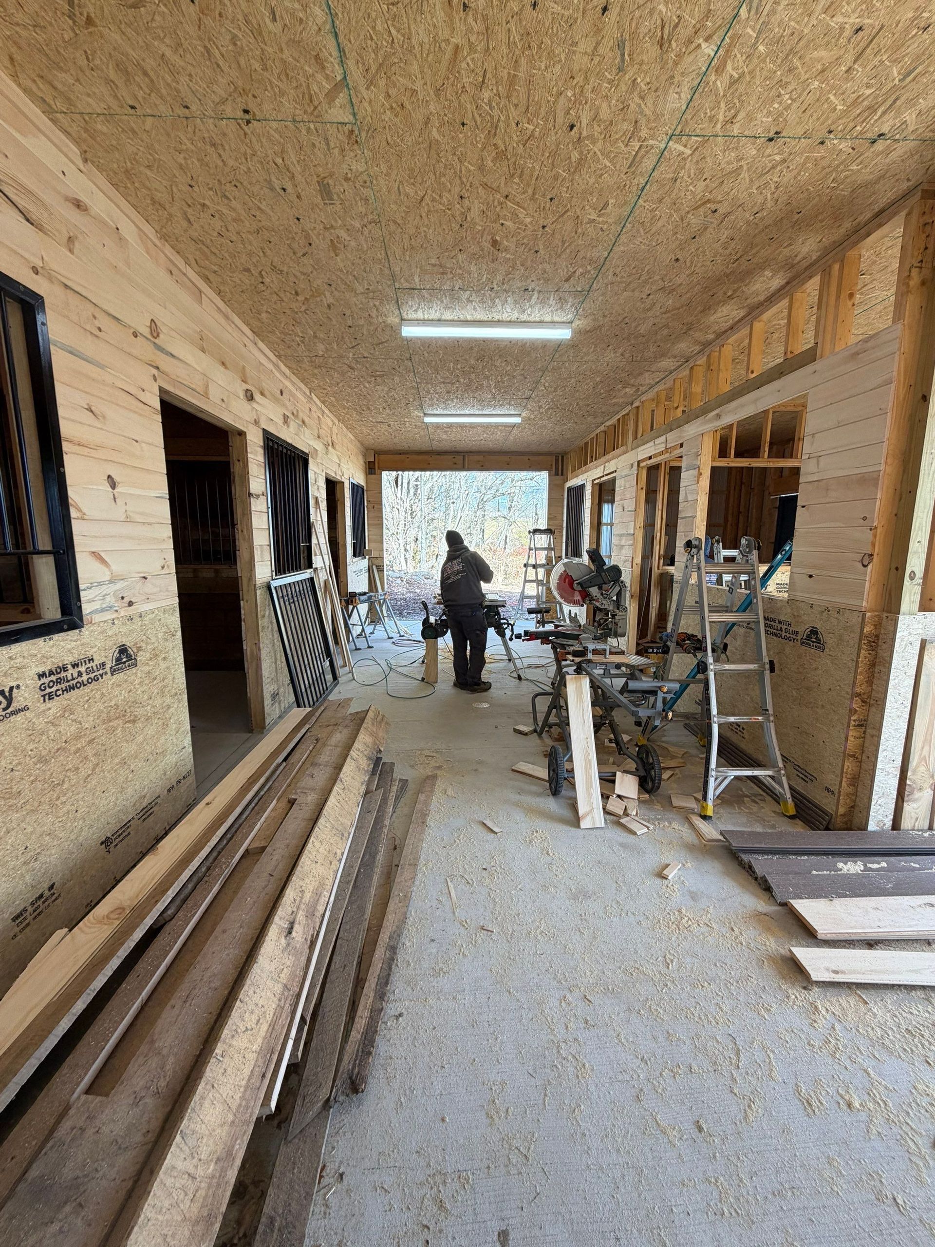 Partially built wooden corridor with construction materials, ladders, and two workers near the far end.