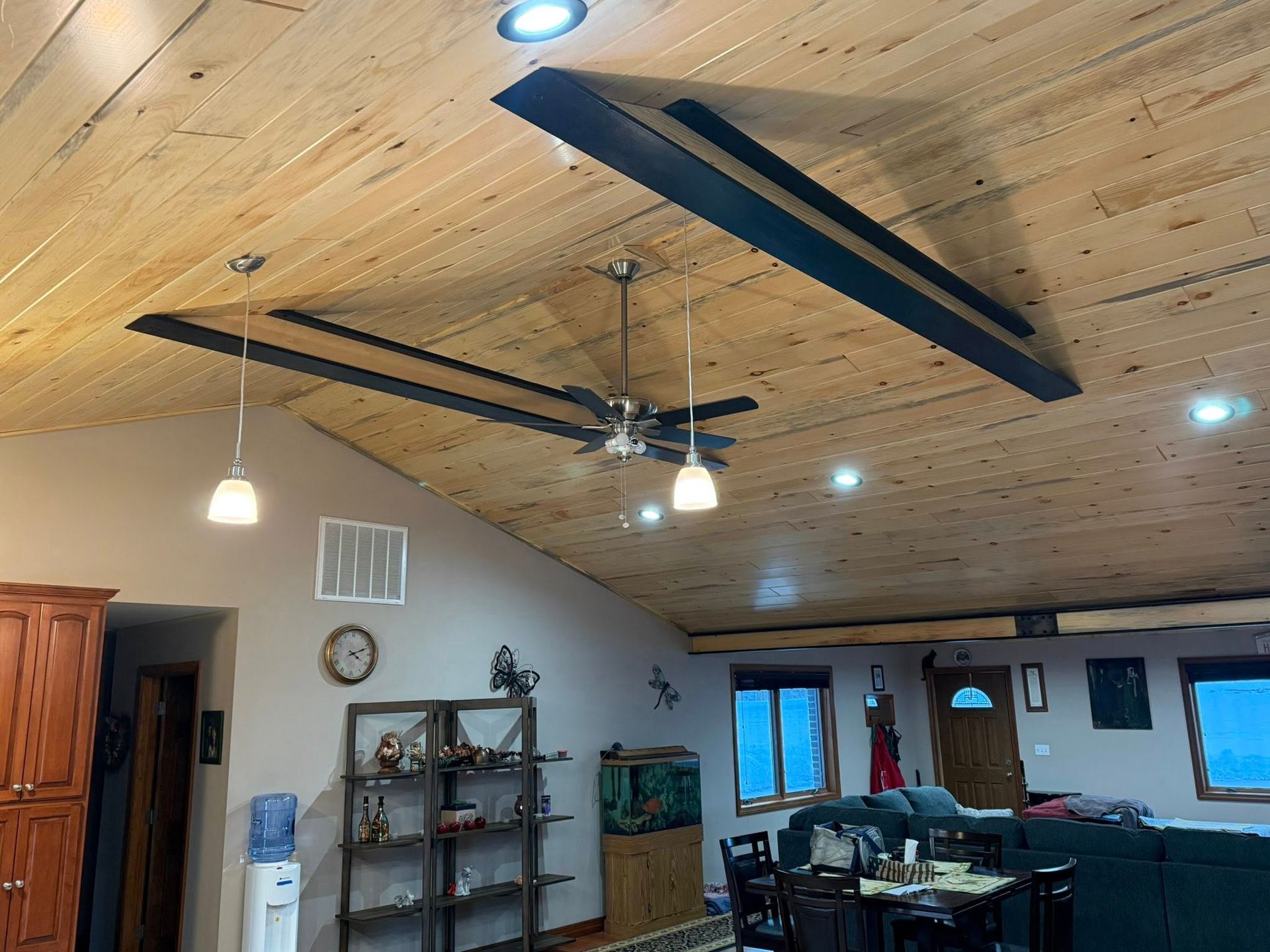 Living room with wood-paneled ceiling, ceiling fans, pendant lights, shelves, and a dining area.