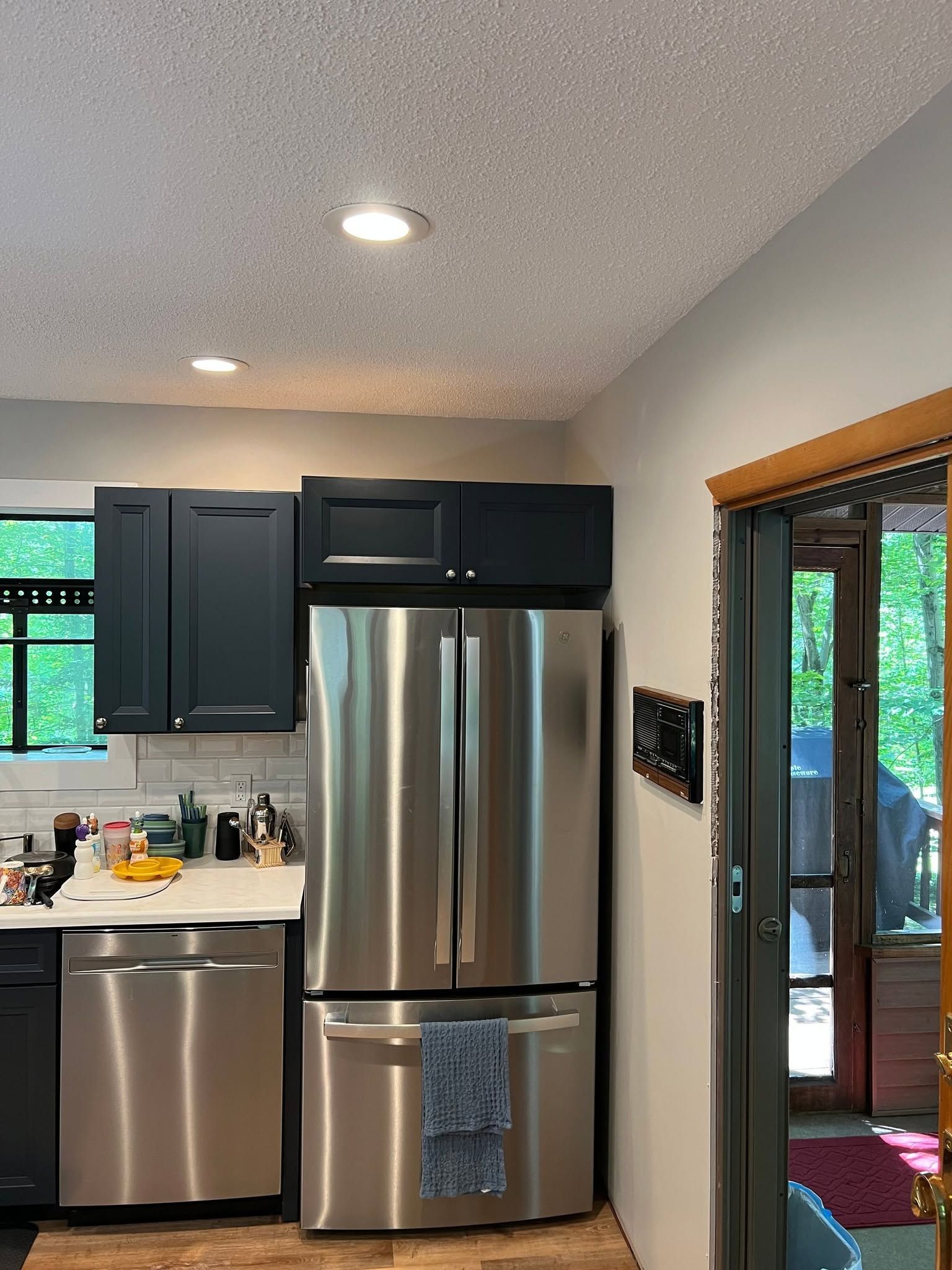 Kitchen with stainless steel refrigerator and dishwasher, dark cabinets, and a door to a patio.