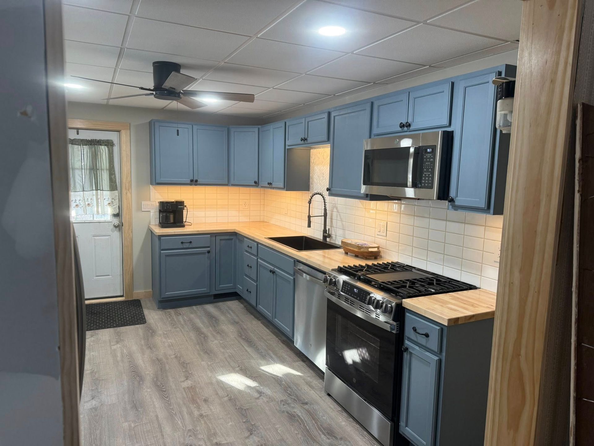 Modern blue kitchen with stainless appliances, wood countertops, white tile backsplash, and gray flooring