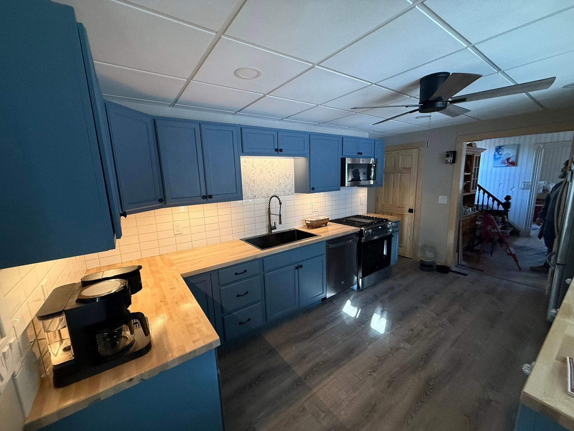 Blue kitchen with cabinets, countertop coffee maker, sink, and dining area in the background