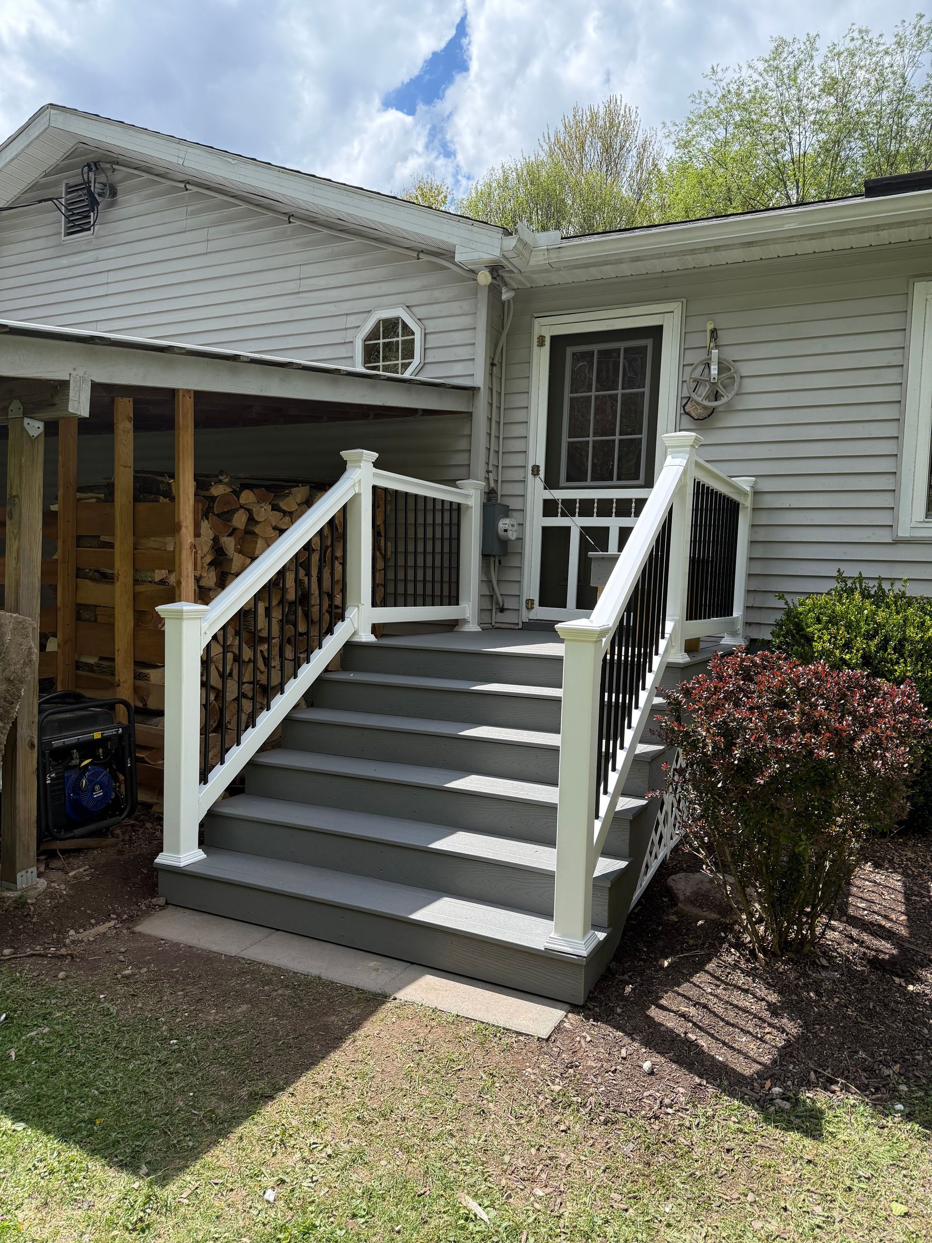 Front porch with gray stairs, white railings, and a screened door on a house exterior