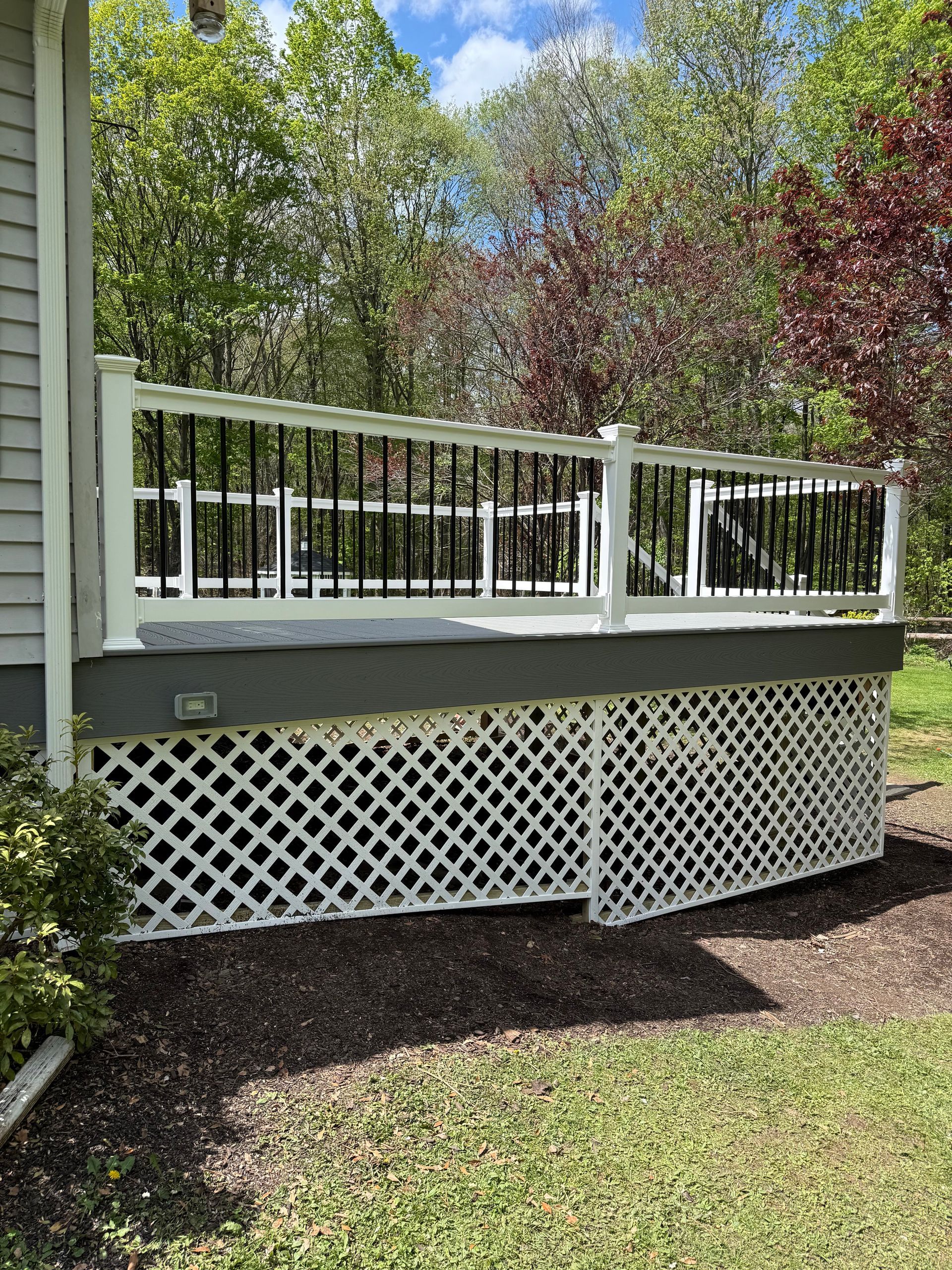 White-railed wooden deck with lattice skirt beside a green yard and trees