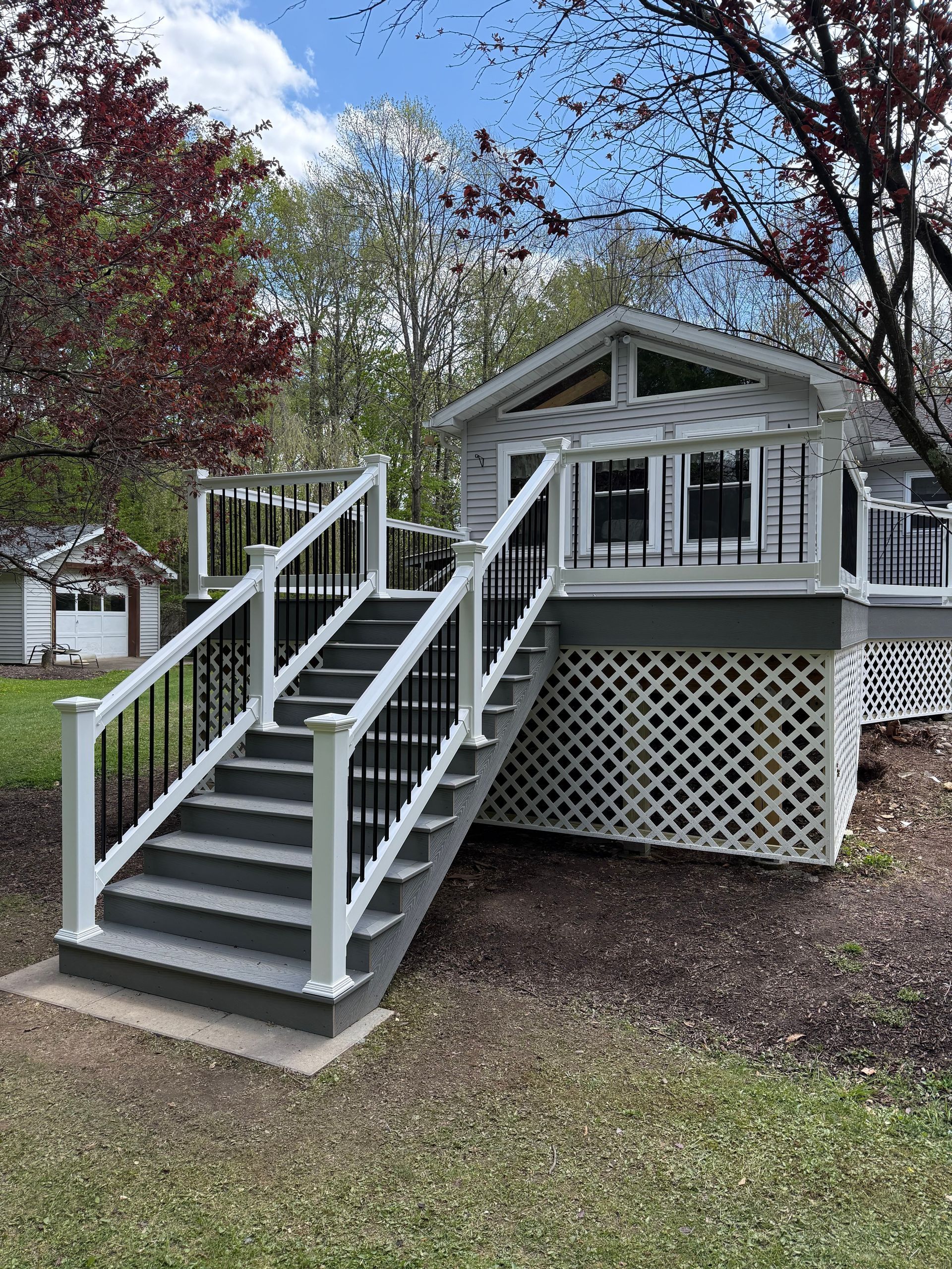 Small house with a gray front porch, white railings, and stairs leading up from a grassy yard.
