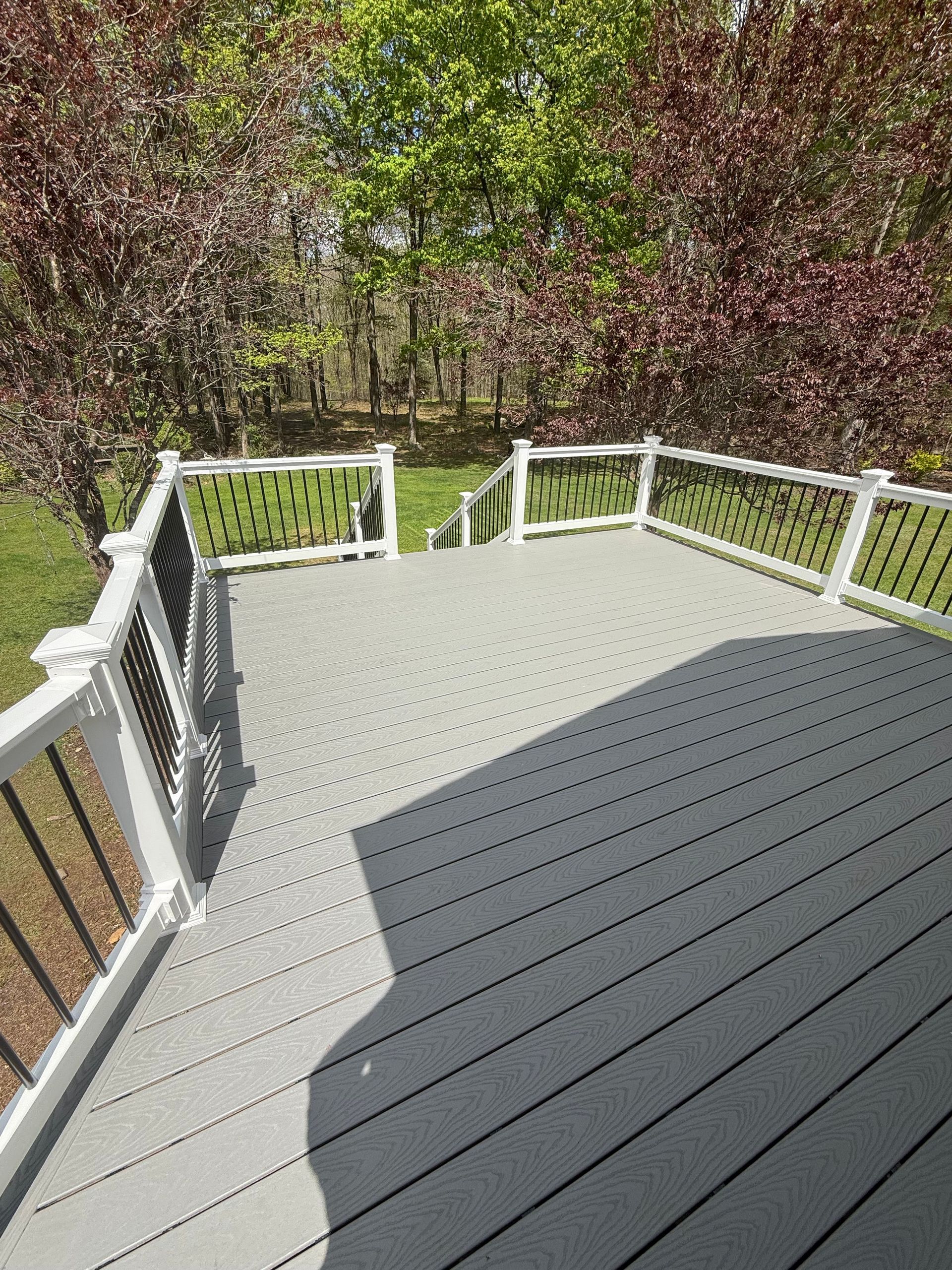 Wooden deck with white railings overlooking a green wooded yard in bright sunlight