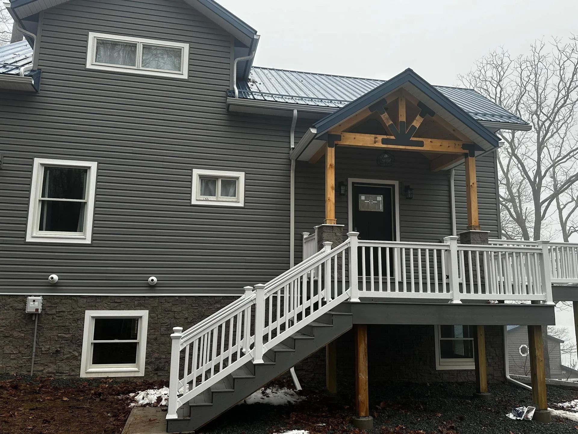 Dark gray house with white trim and an elevated front porch with stairs in winter.