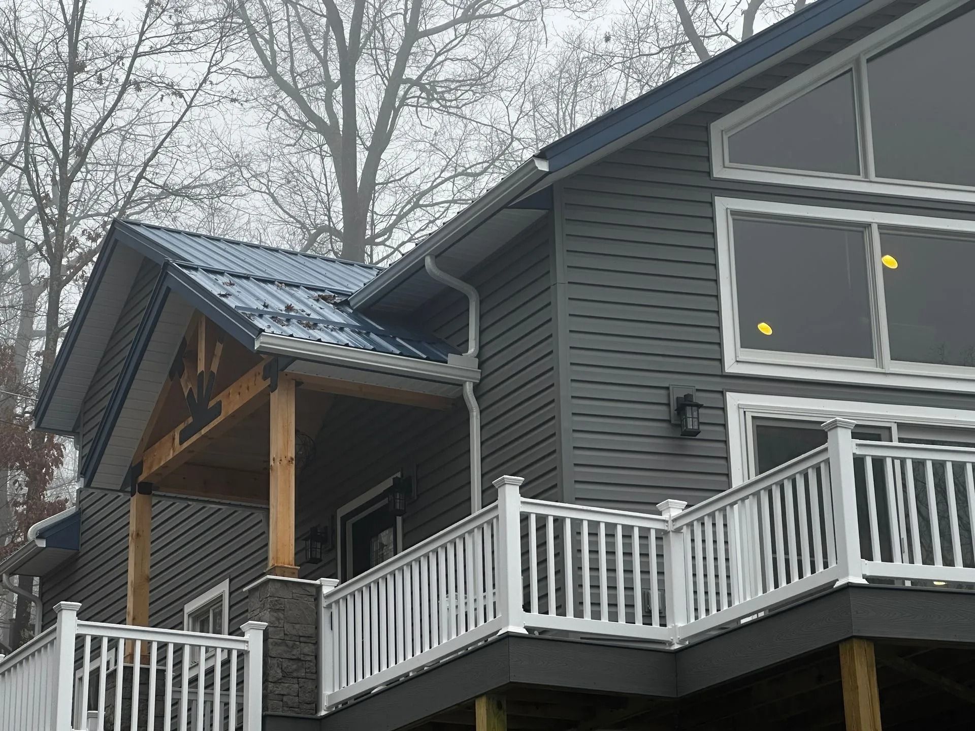 Modern gray house with white railings and a covered porch on a wooded hillside