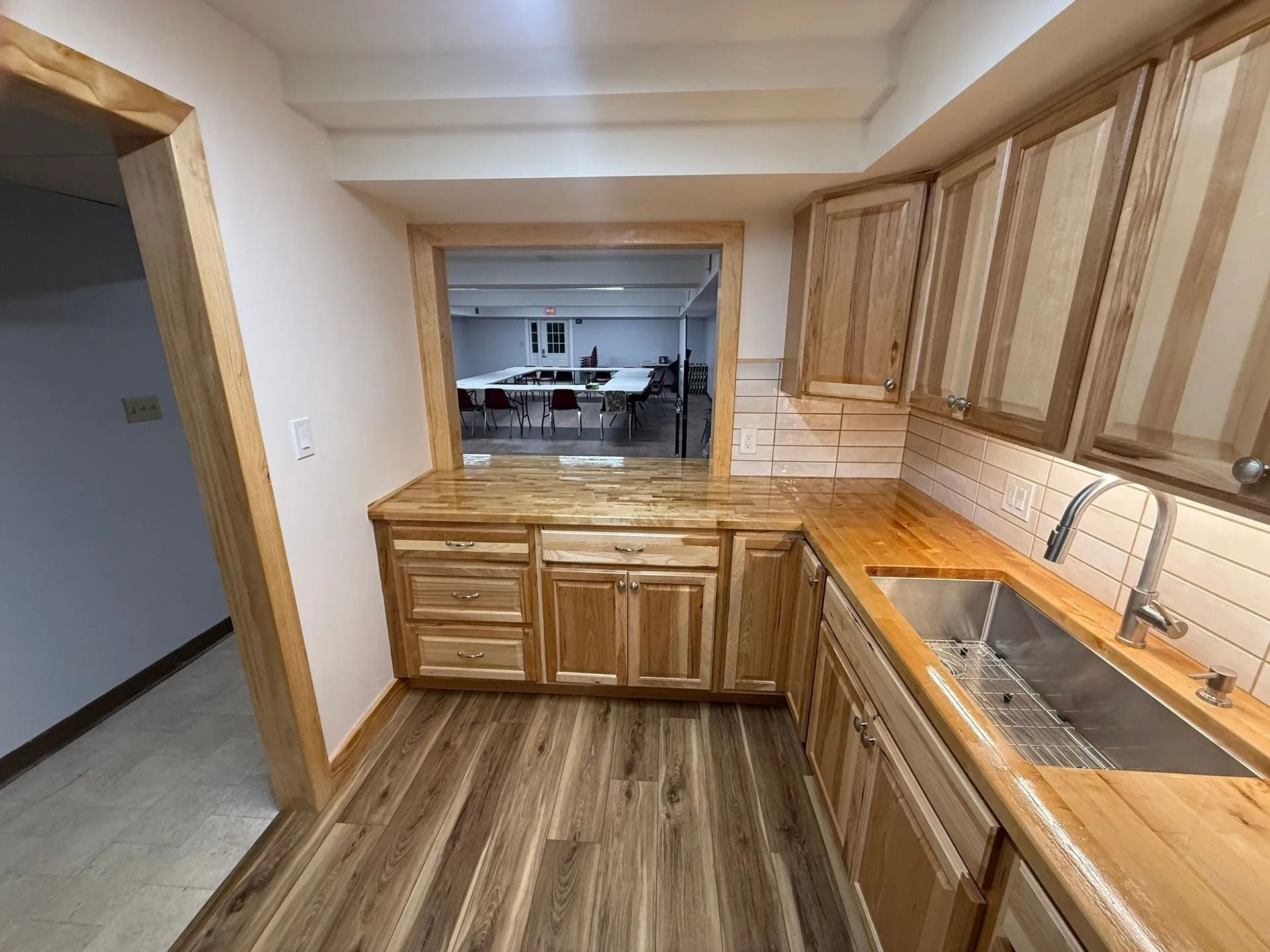 Small kitchen with wood cabinets, countertop sink, and a pass-through opening to another room.