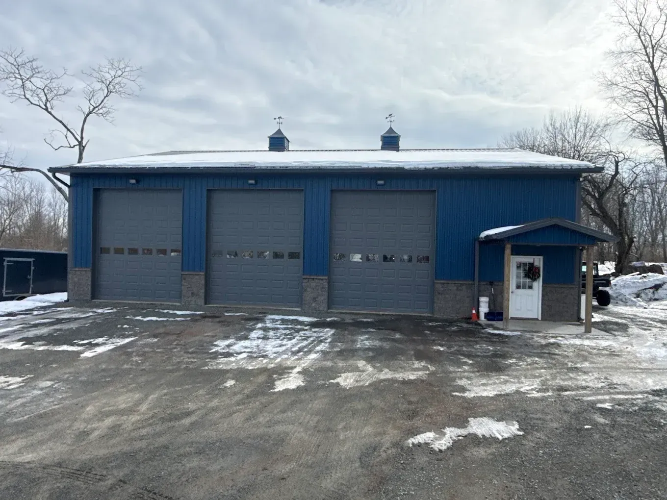 Blue garage with three bay doors and a small side entrance on a snowy lot