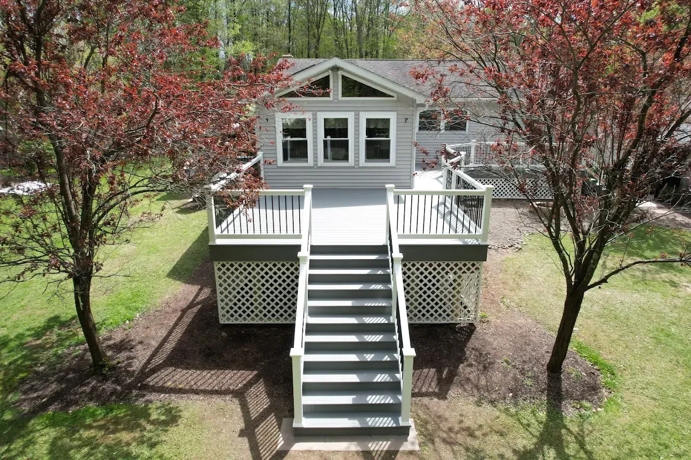 Small white house with front porch, stairs, and blooming trees in a yard