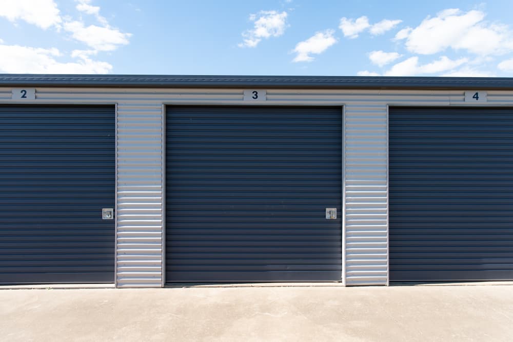 Storage units, three dark blue doors with white trim, set in front of a blue sky. — Bay & Basin Storage In Huskisson, NSW