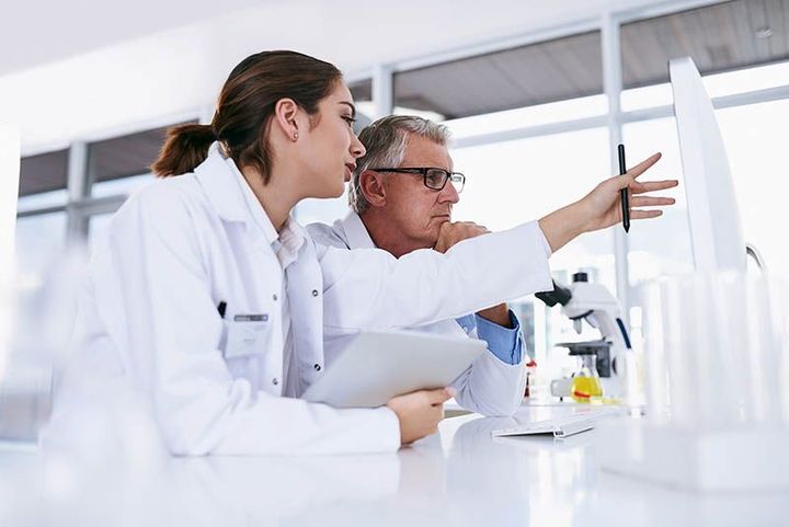 Scientists in white lab coats examining equipment in a bright laboratory