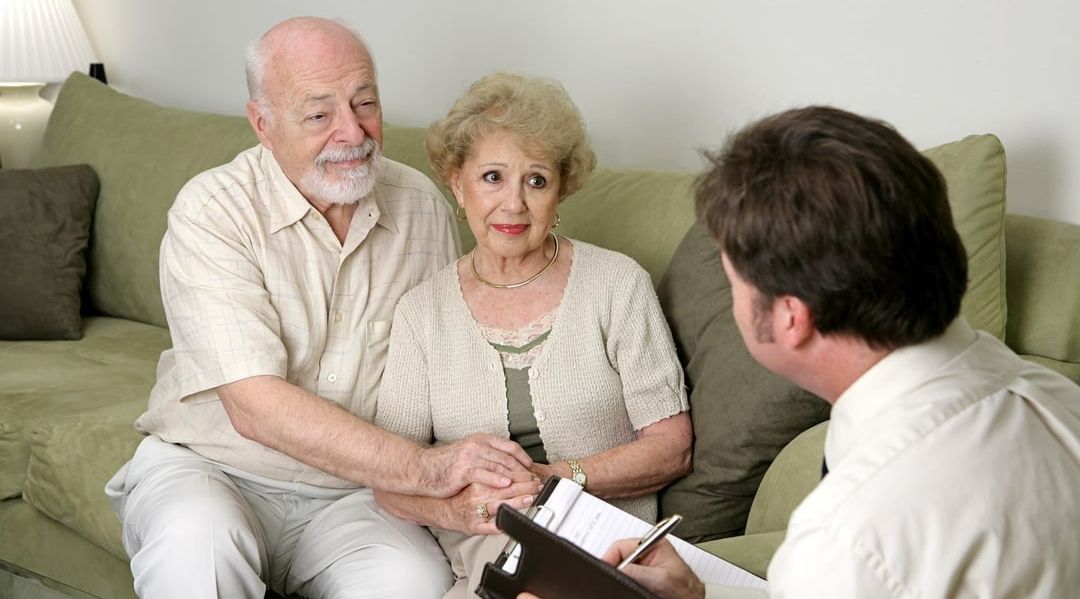 older couple sitting on a couch with a younger man writing