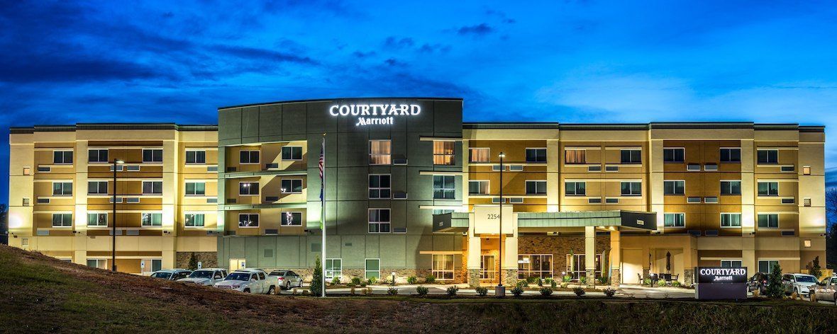 Courtyard by Marriott hotel exterior at dusk. Buildings lit with lights. Dark blue sky.