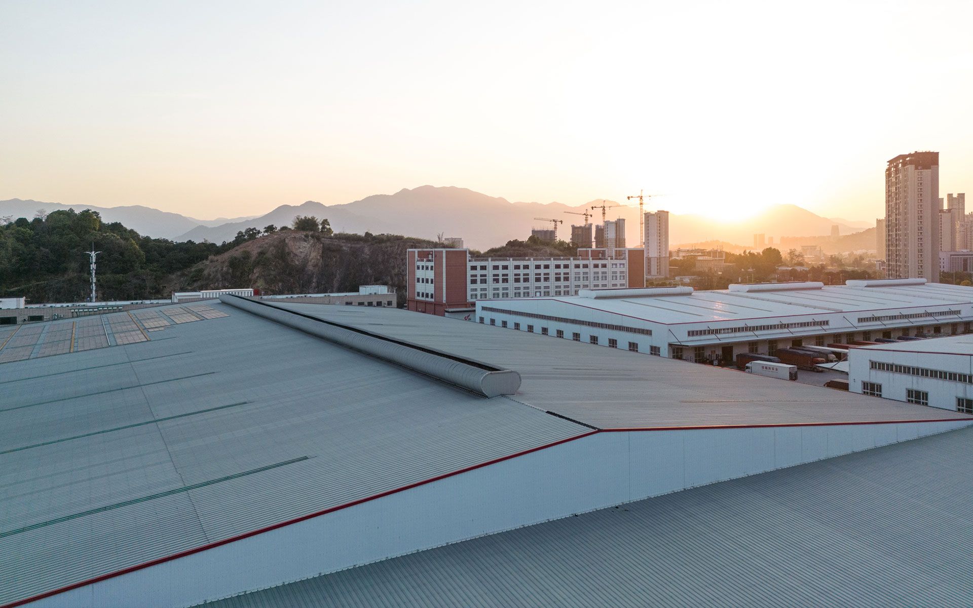An aerial view of a large building with a roof at sunset.