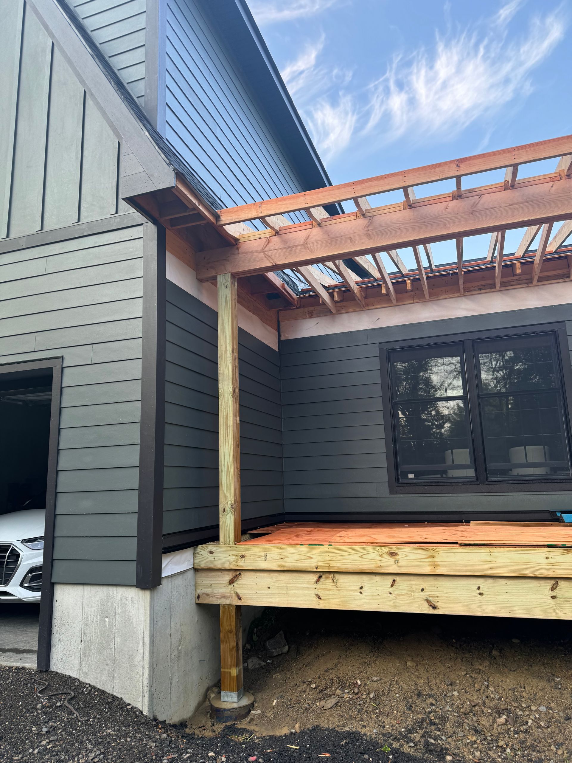 A car is parked in a garage next to a house under construction.