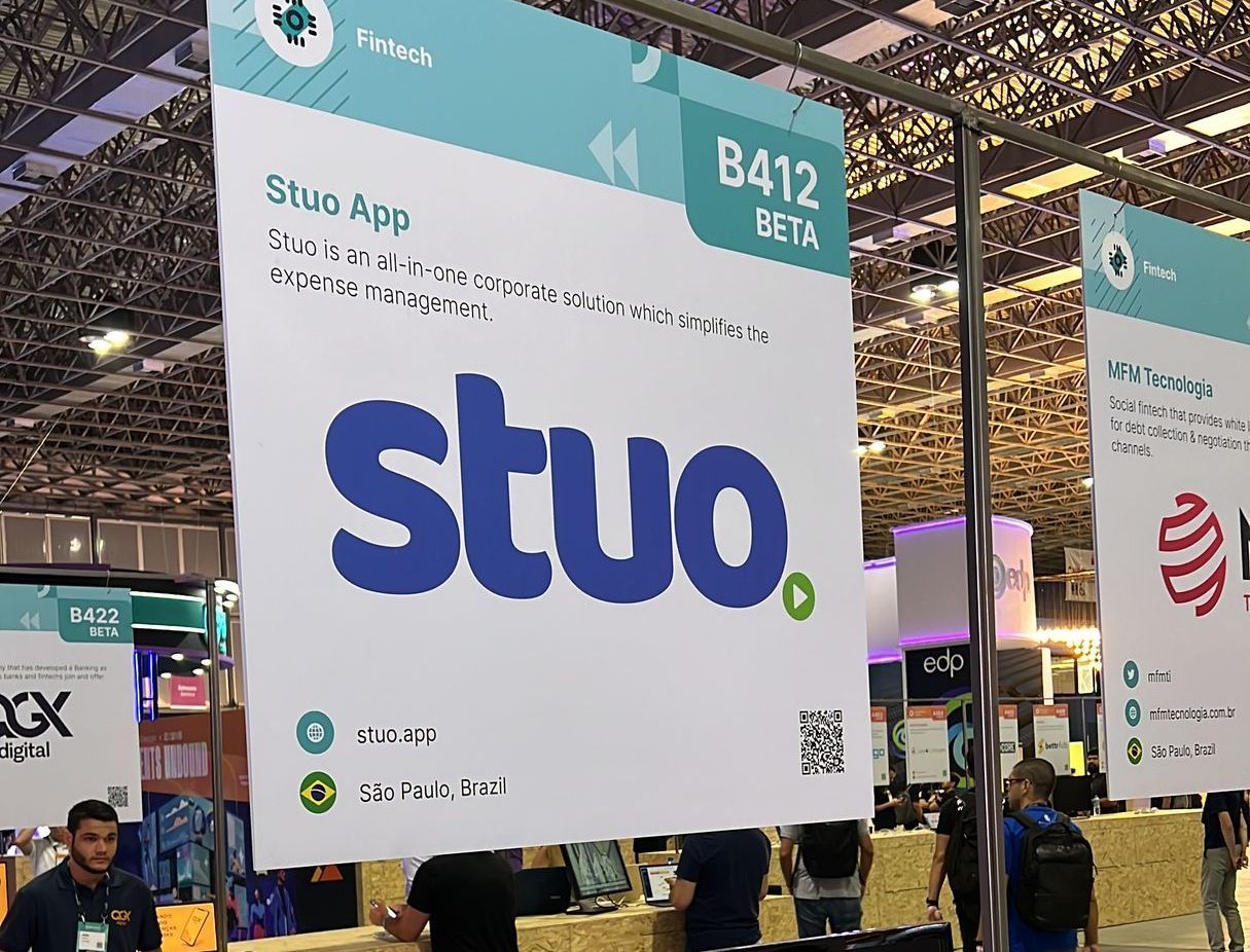Stuo app booth at an expo, with a large white sign and blue logo under a convention hall ceiling.