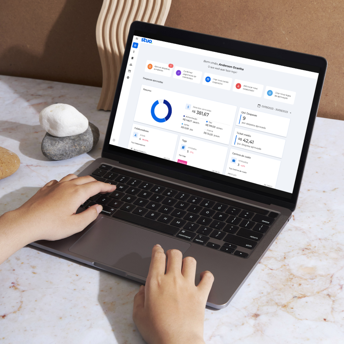 Hands using a laptop on a marble desk, showing a dashboard on the screen