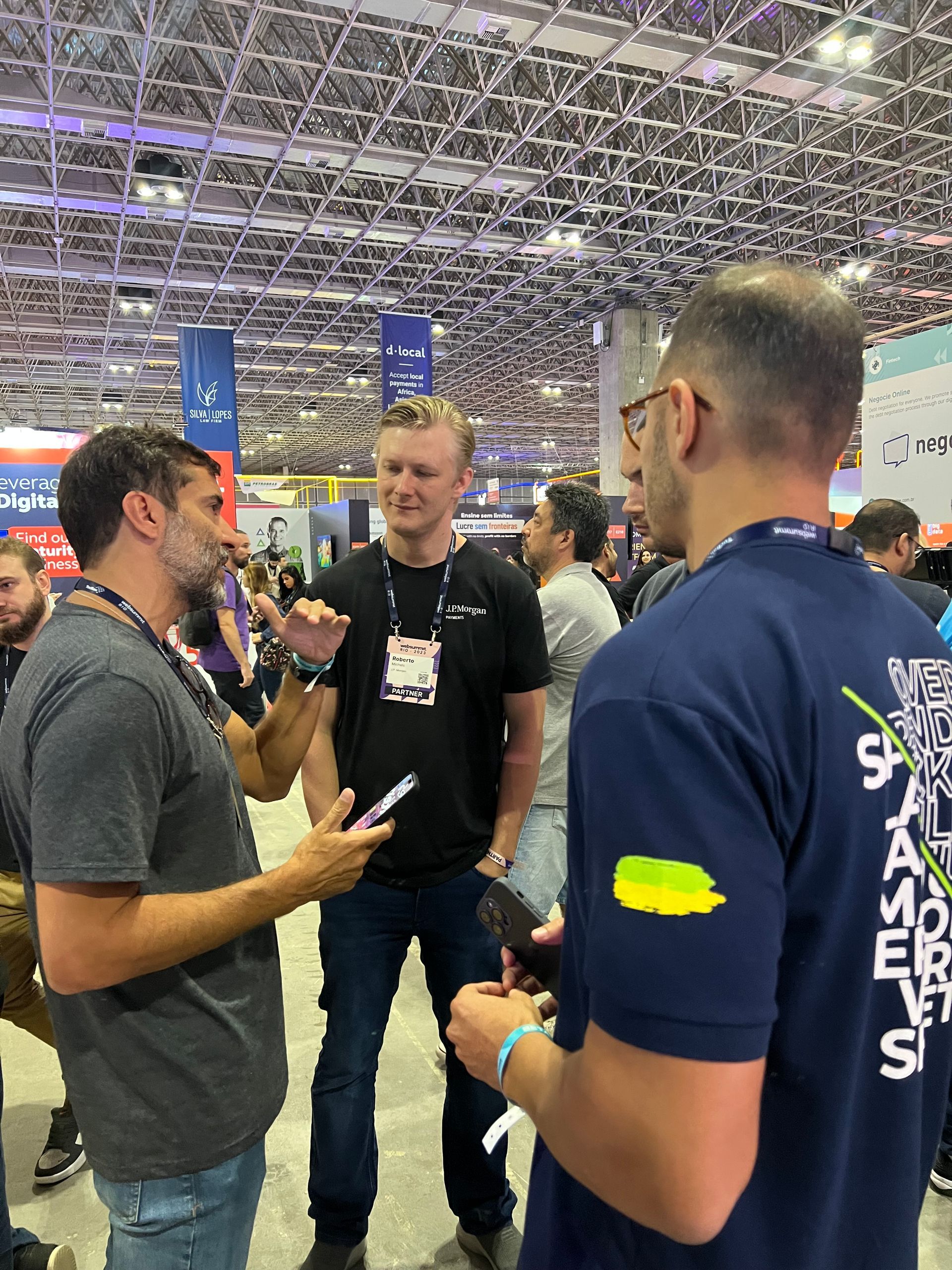 Three people chatting at a trade show booth under a bright ceiling.