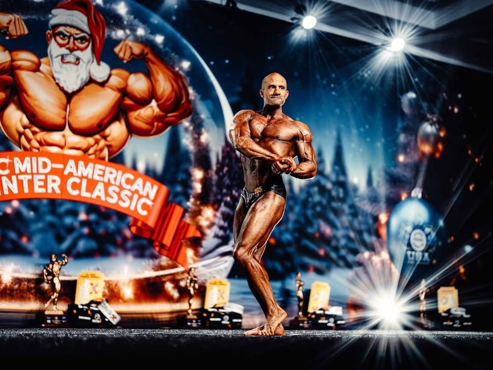 Bodybuilder posing on a stage with bright spotlights and a large “Mid-America Center Classic” backdrop.