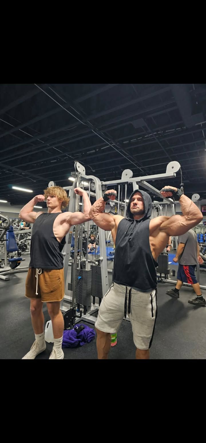 Three gym-goers posing with dumbbells overhead in a crowded fitness center