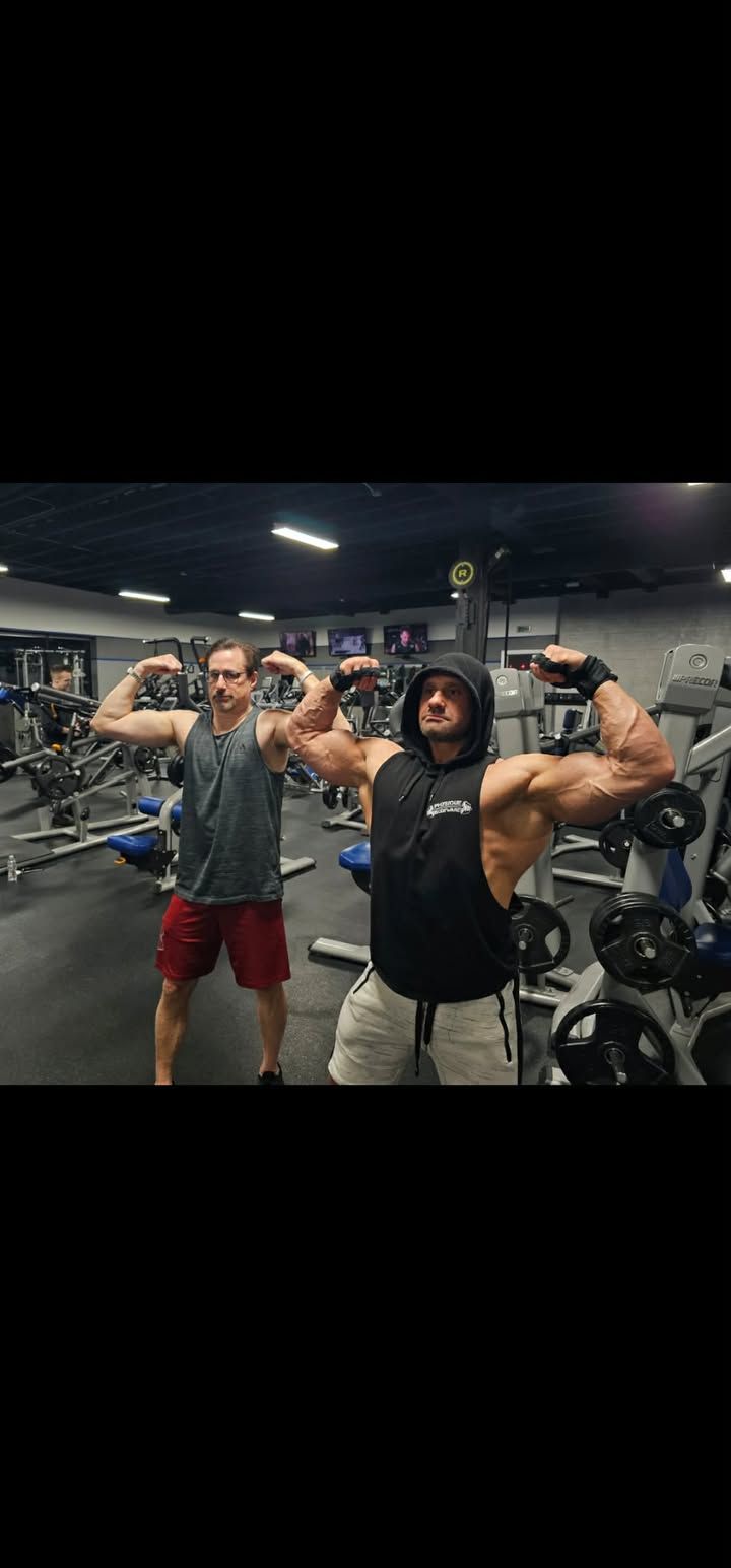 Three people flexing in a gym, posing between weight machines under bright overhead lights.