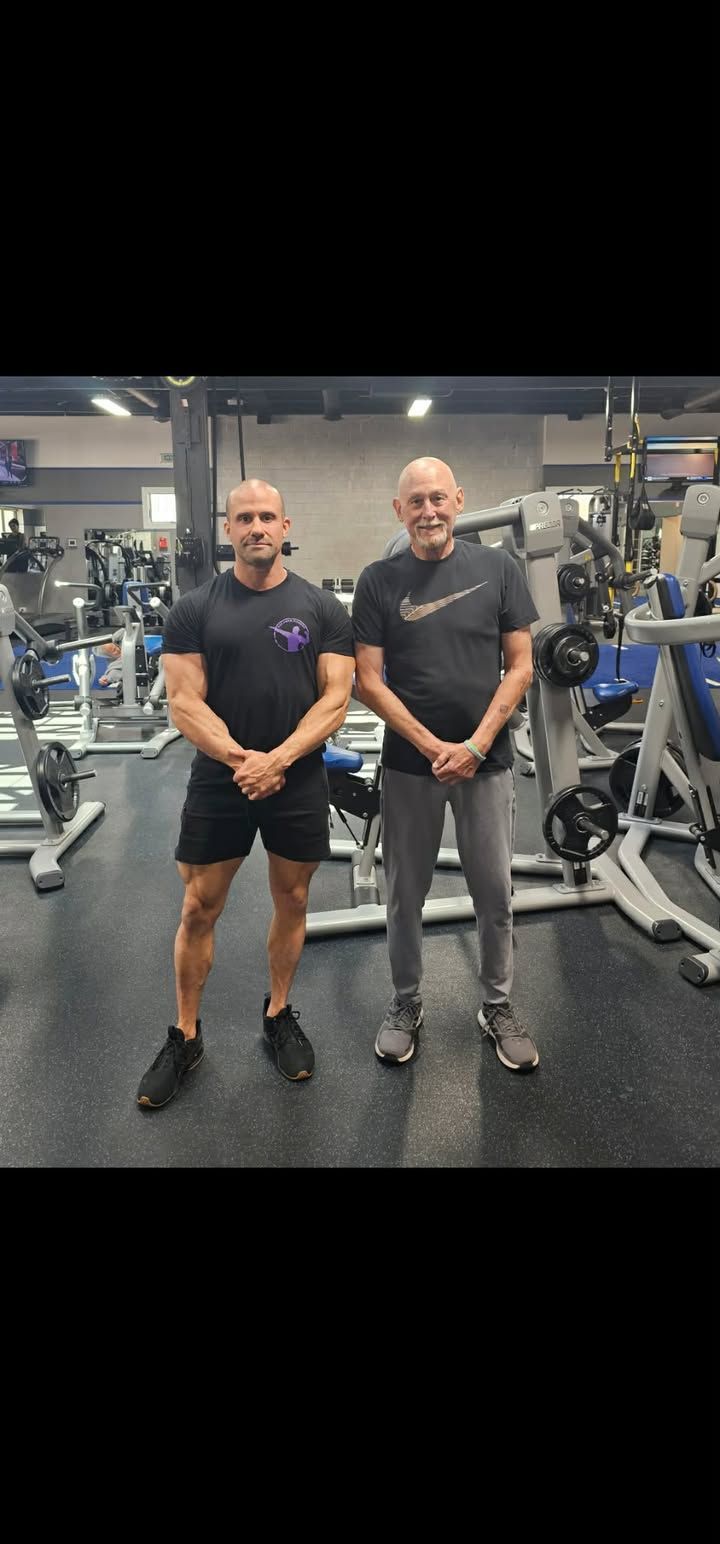 Two men standing side by side in a gym, posing between weight machines.