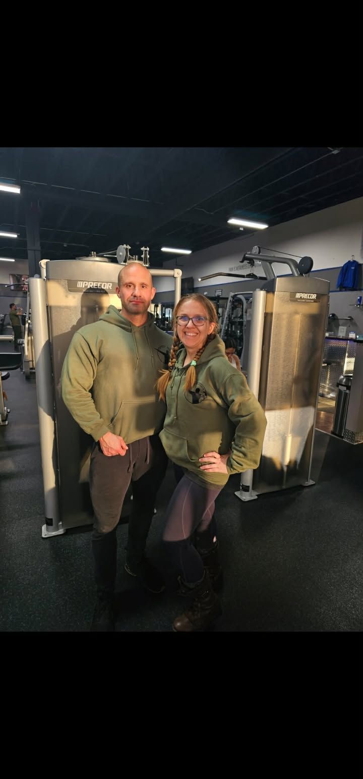 Two people posing together in a dim industrial setting with stainless steel tanks in the background