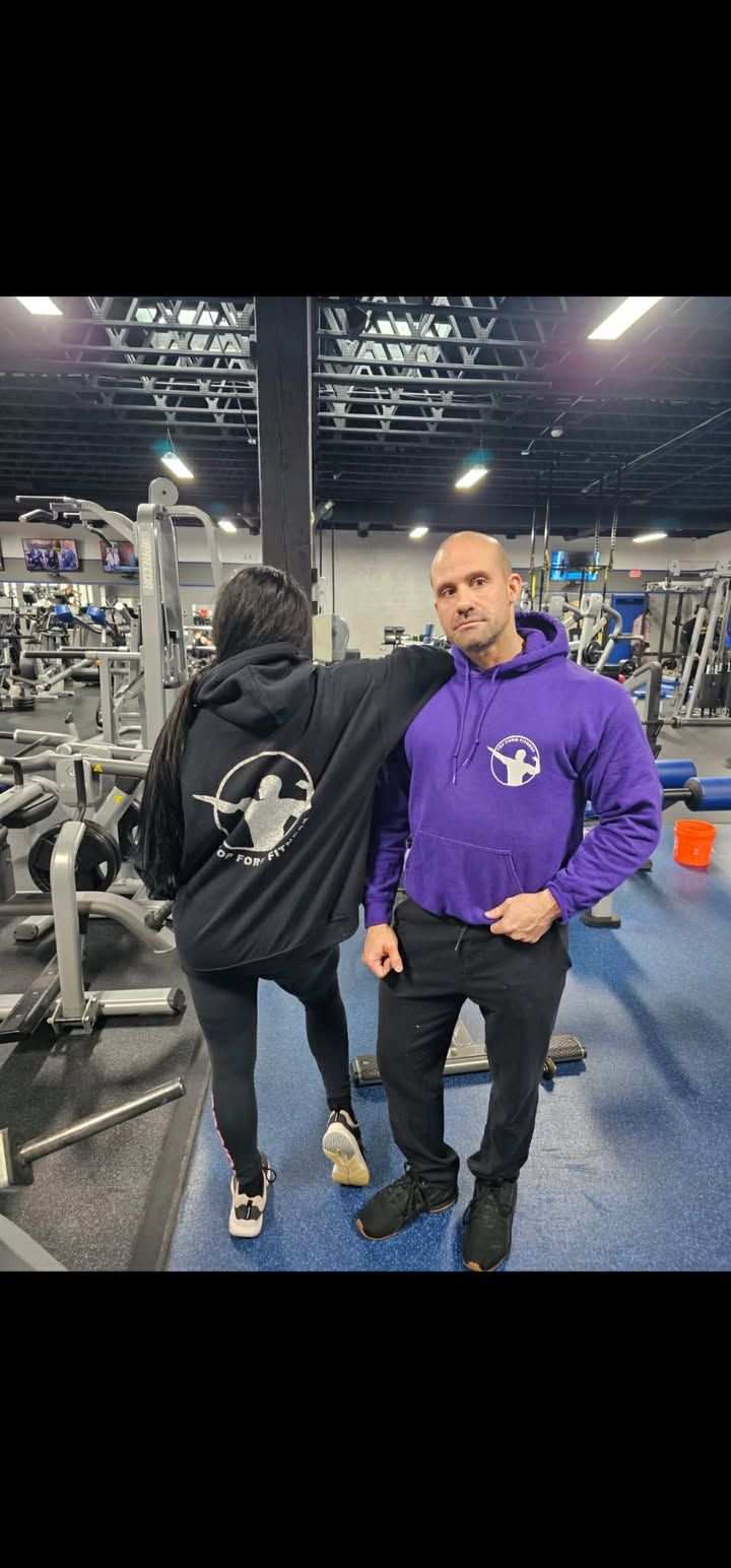 Two men in hoodies stand in a gym, one facing away and one in a purple sweatshirt