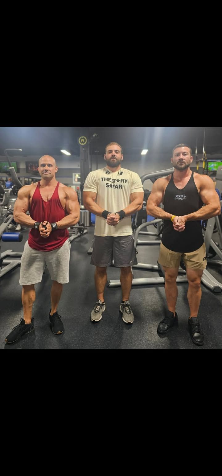 Three men pose in a gym, holding medals and standing shoulder to shoulder.
