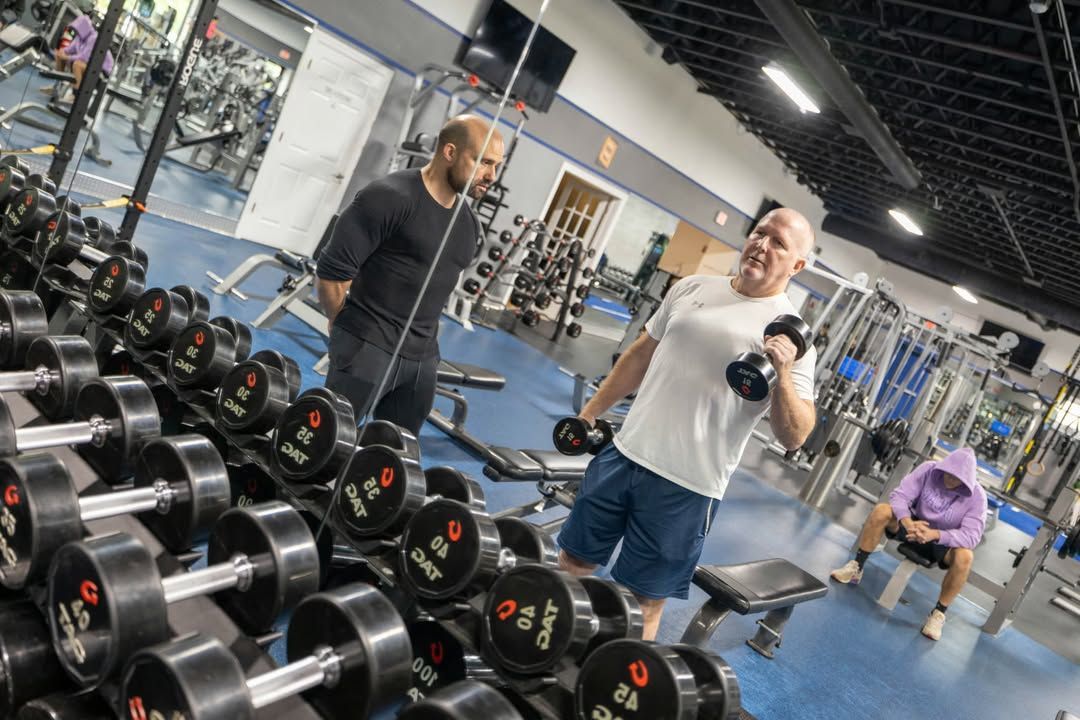 People lifting dumbbells in a gym near a rack of weights