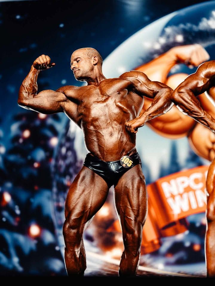 Bodybuilder flexing on a stage with orange and blue lights and an NPC WIN banner in the background