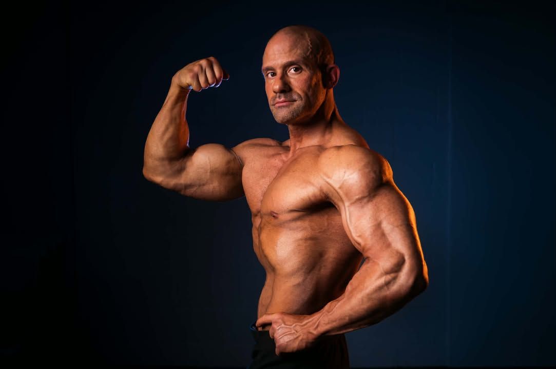 Muscular man posing with flexed arm against a dark background
