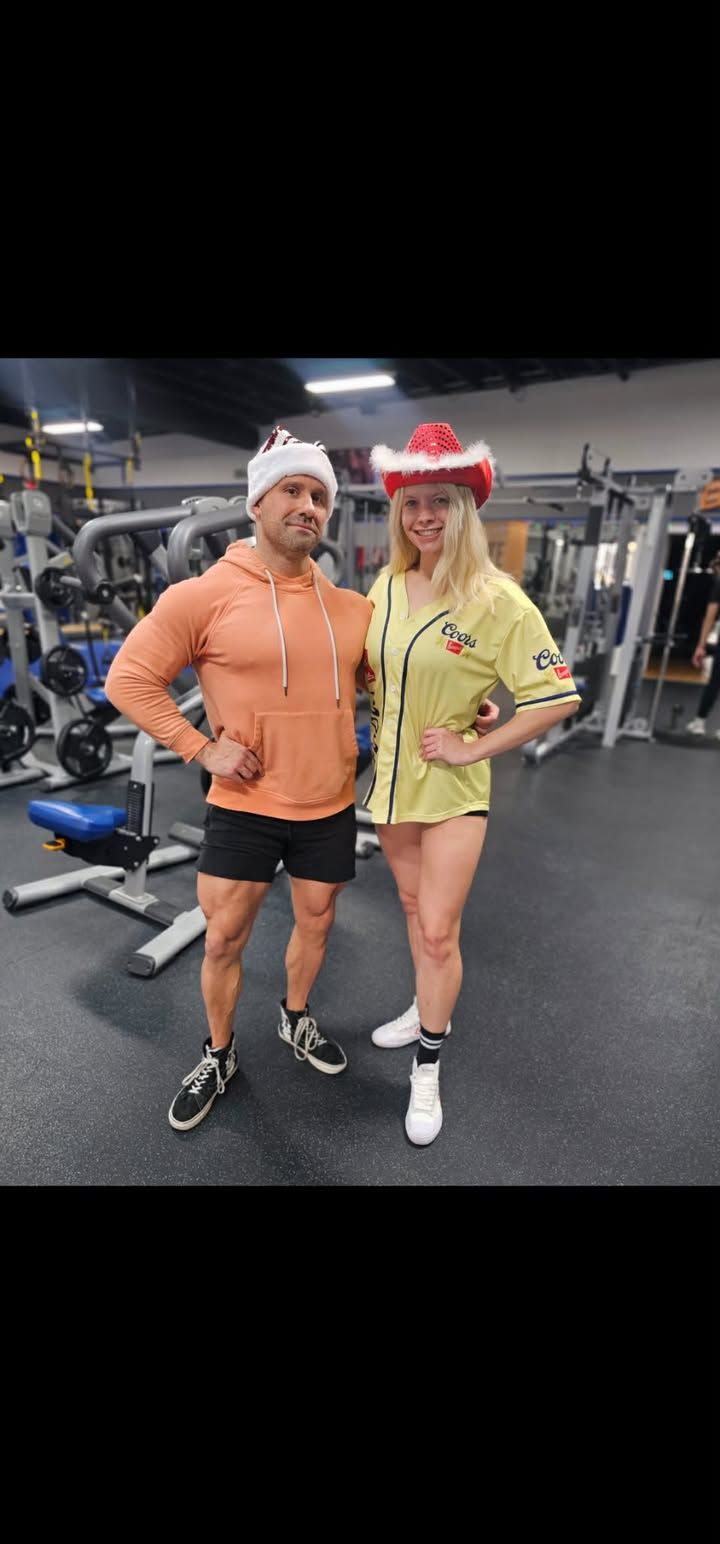 Two people posing in a gym, wearing bright workout clothes and festive hats.
