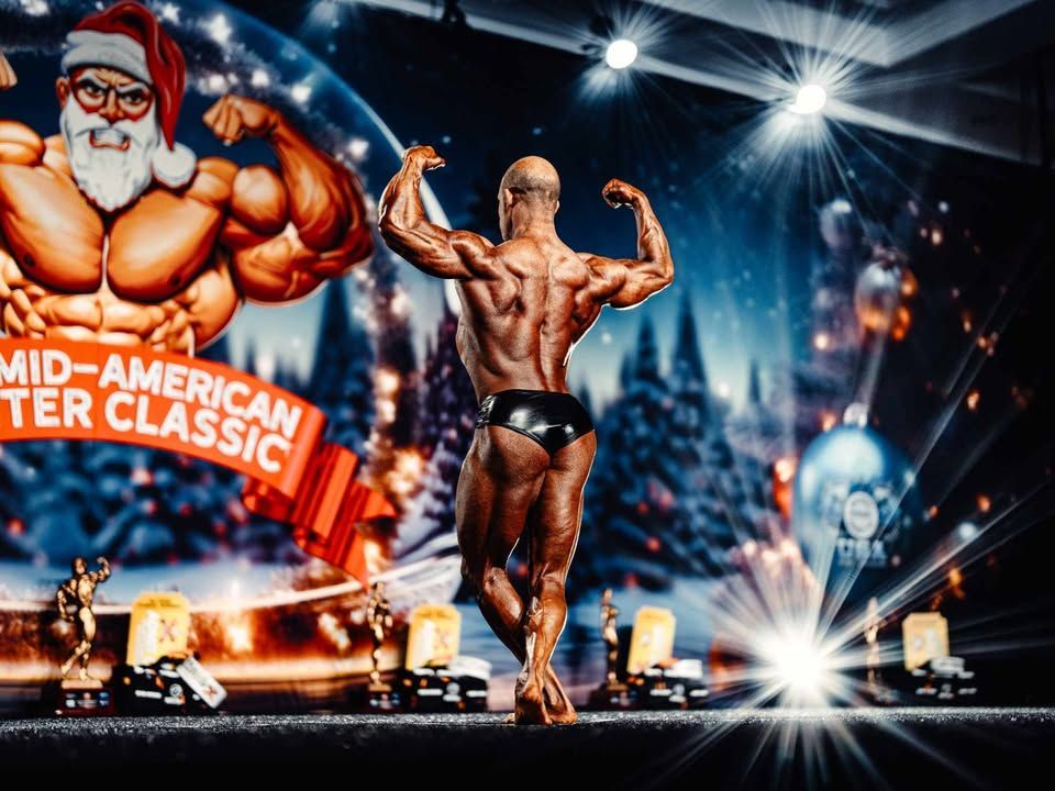 Bodybuilder posing on stage under bright lights at the Mid-America Winter Classic event