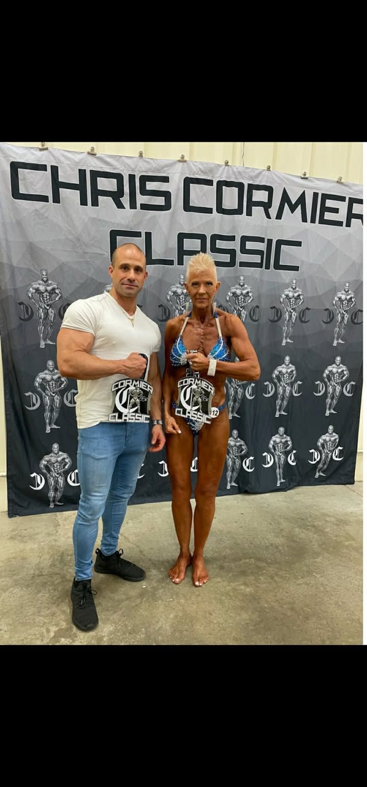 Two people posing in front of a Chris Cormier Classic backdrop, holding trophies and medals.