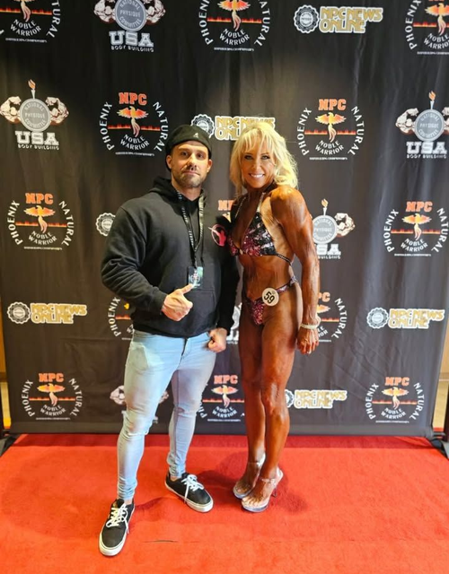 Two people pose on a red carpet in front of a branded event backdrop.