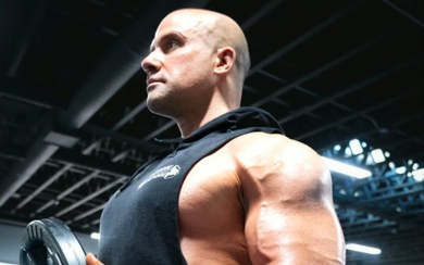 Muscular man lifting a dumbbell in a gym, viewed from the side under bright overhead lights