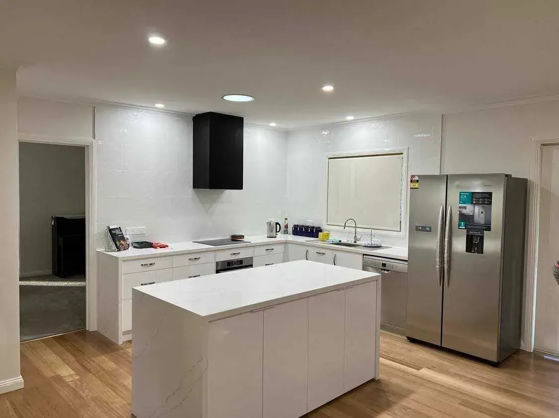Bright modern kitchen with white cabinets, island, stainless steel fridge, and hardwood floor
